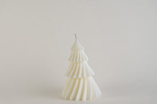 Candela natalizia piccola a forma di albero di Natale, vista frontalmente su sfondo chiaro.