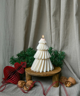 Candela grande a forma di albero di Natale, accesa e vista frontalmente, con decorazioni natalizie e schiaccianoci sullo sfondo.