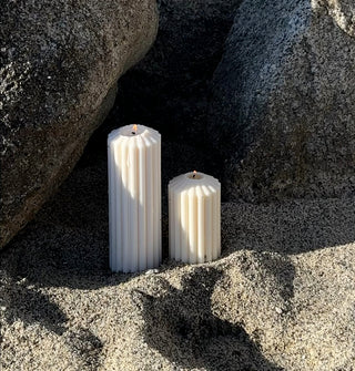 Candela a colonna color avorio sulla sabbia, tra le rocce, in una scena di spiaggia.