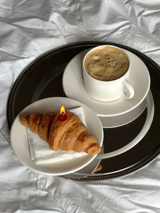 Candela a forma di croissant accesa accanto a una tazza di caffè.