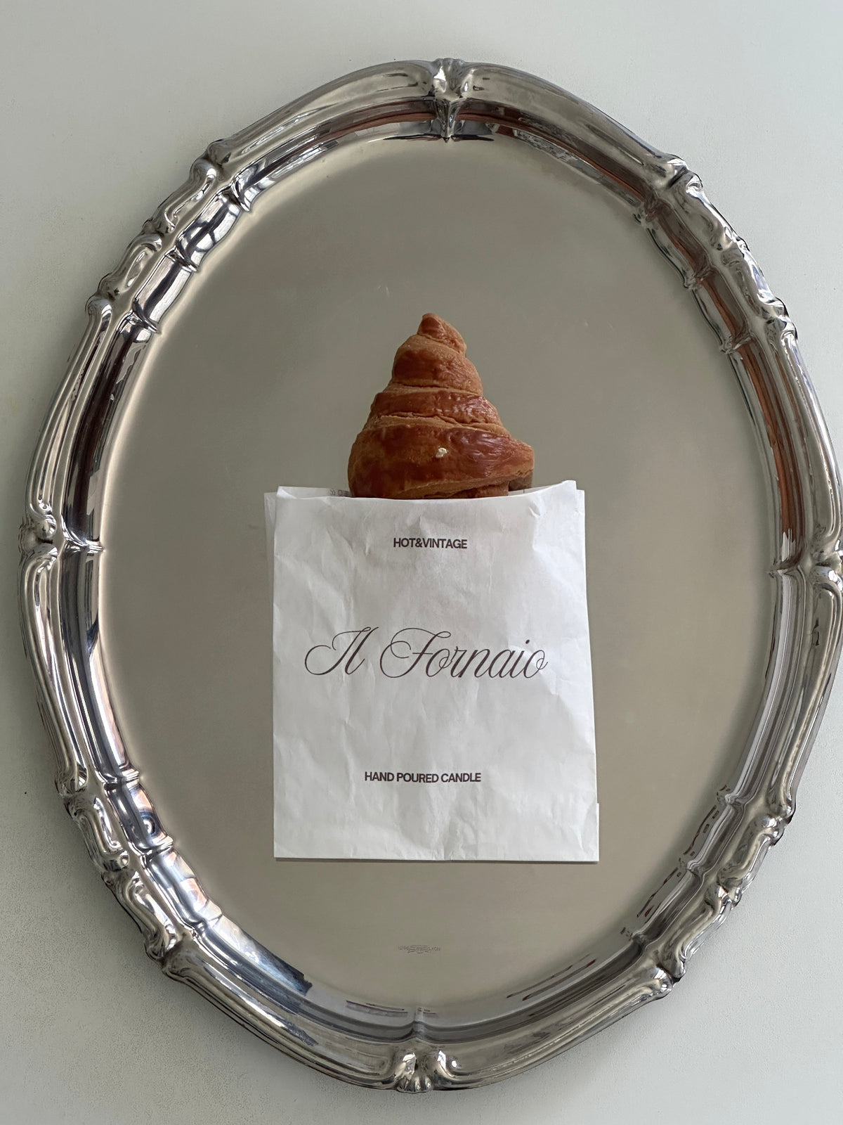 Candela a forma di croissant nel sacchetto personalizzato Il Fornaio, su un piatto argentato.