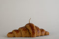 Candela Croissant a forma di cornetto dorato con stoppino, vista laterale su fondo grigio chiaro