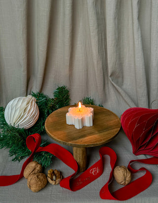 Candela a forma di fiocco di neve accesa su un tavolo di legno con decorazioni natalizie e nocciole.