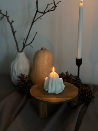 Candela di Halloween a forma di fantasma grande accesa su un tavolo con zucca e pinoli.