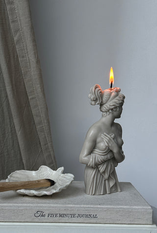Candela Lady Aphrodite color grigio pietra accesa, appoggiata su un libro.