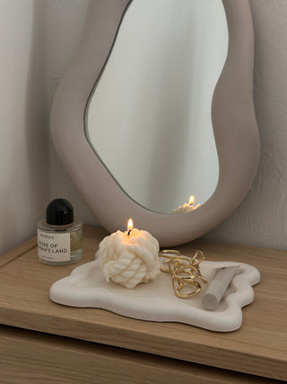 Candela a forma di nodo su un piattino color crema con dettagli dorati.