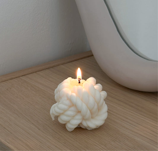 Candela profumata a forma di nodo appoggiata su un mobile in legno davanti a uno specchio.