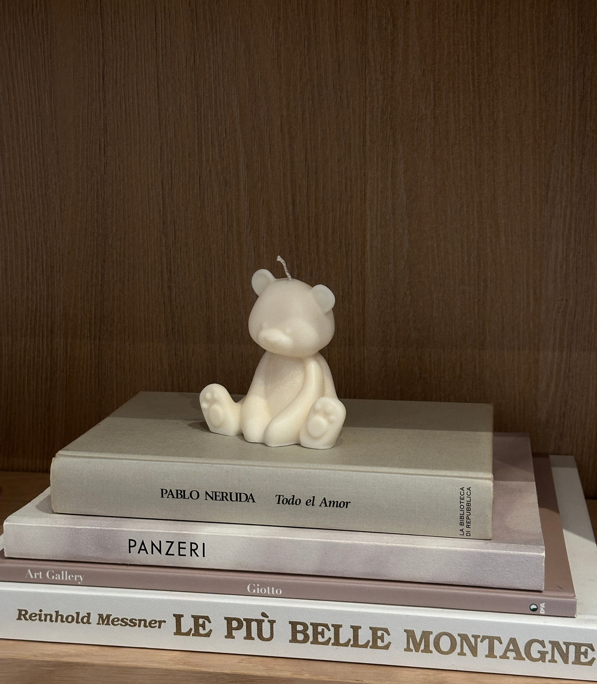 Candela a forma di orsetto appoggiata su alcuni libri davanti a una libreria marrone.
