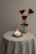 Candela color avorio a forma di peonia su un tavolino con rose, nella luce del pomeriggio.