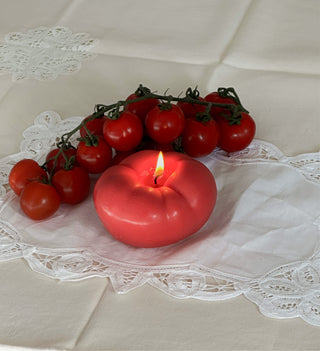 Candela a forma di pomodoro accesa, circondata da pomodori freschi.