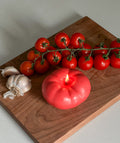 Candela a forma di pomodoro su un tagliere, con aglio e pomodori freschi.