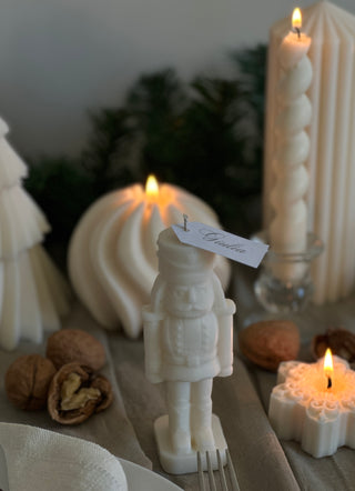 Candela a forma di schiaccianoci su una tavola natalizia apparecchiata, tra decorazioni e altre candele.