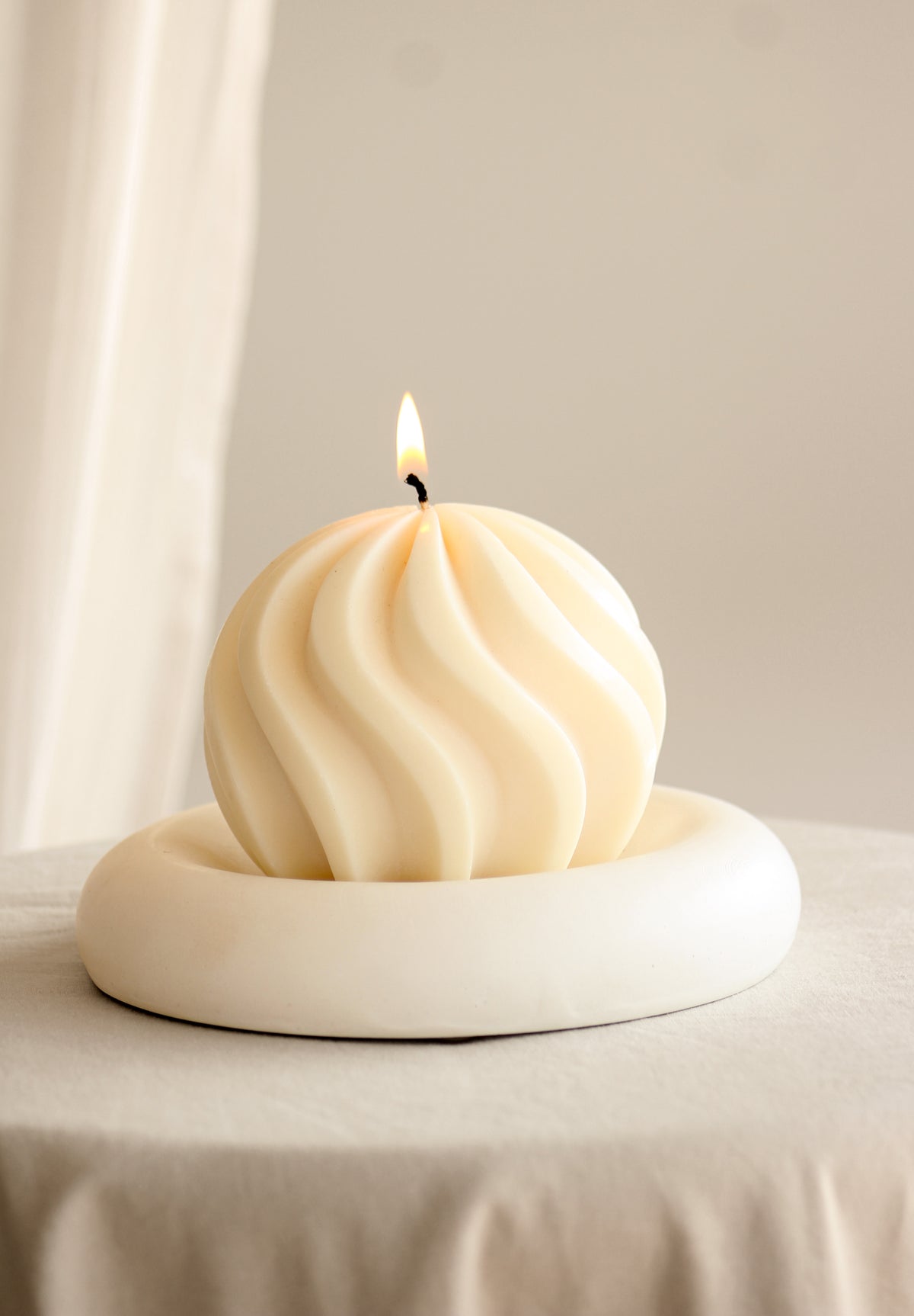 Candela a sfera grande con spirale avorio, accesa in una composizione con altre candele, frutta, noci e un bicchiere su una tavola apparecchiata.