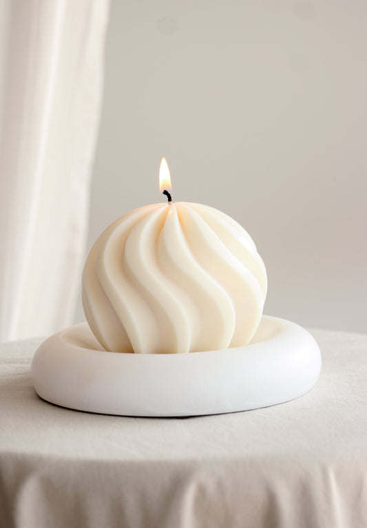 Candela a sfera grande con spirale avorio, accesa in una composizione con altre candele, frutta, noci e un bicchiere su una tavola apparecchiata.