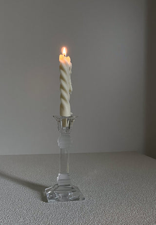 Candela sottile a spirale accesa su un portacandela di vetro, in una scena dai toni scuri.