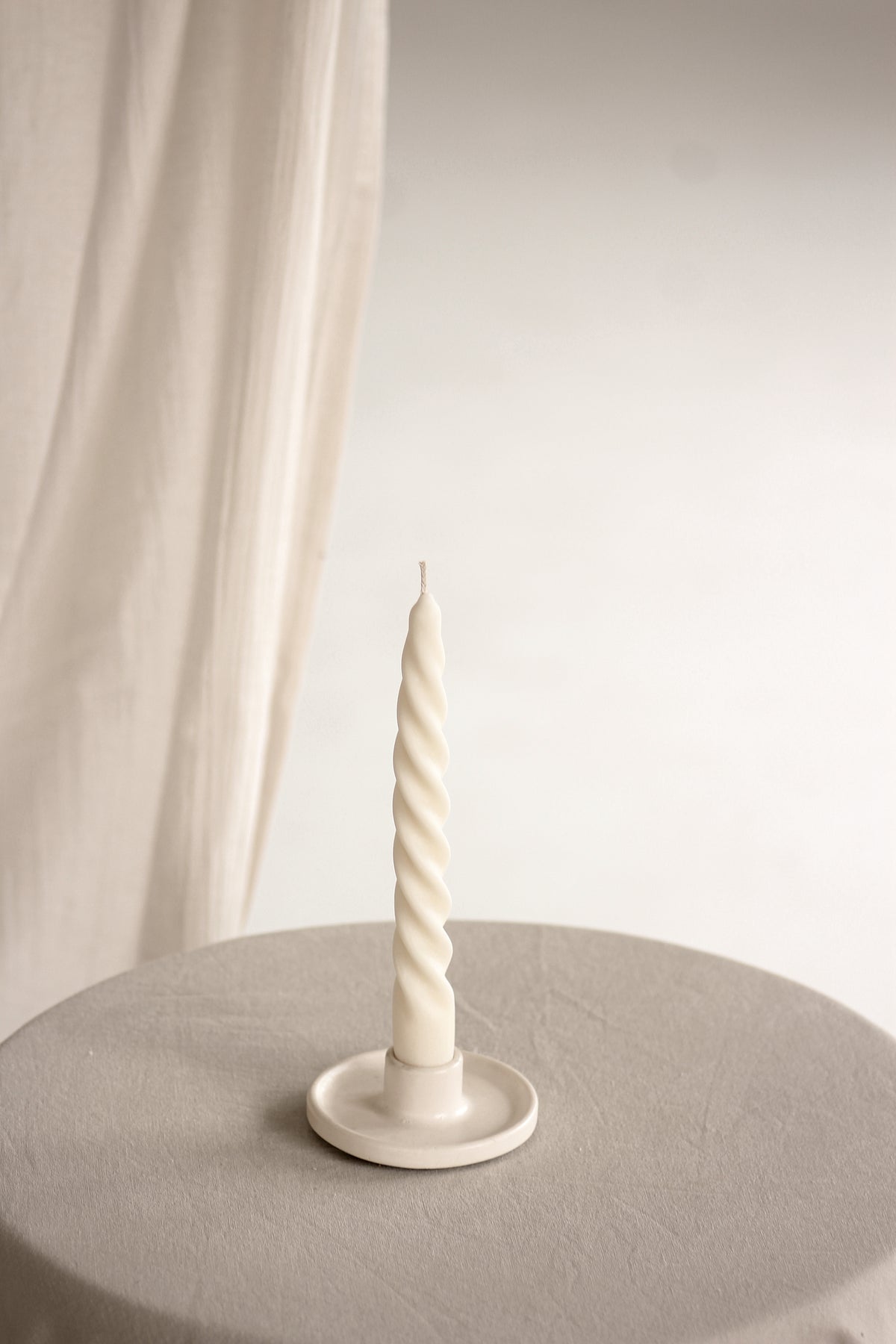 Candela sottile a spirale su un portacandela, appoggiata su un tavolo chiaro con sfondo bianco.
