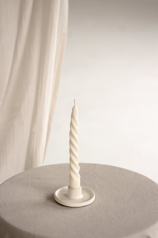 Candela sottile a spirale su un portacandela, appoggiata su un tavolo chiaro con sfondo bianco.