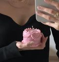 Una persona con un abito nero tiene in mano una candela rosa a forma di torta.