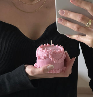Una persona con un abito nero tiene in mano una candela rosa a forma di torta.