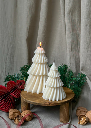 Candele a forma di albero di Natale di diverse dimensioni, con quella grande accesa, in un allestimento festivo con schiaccianoci.