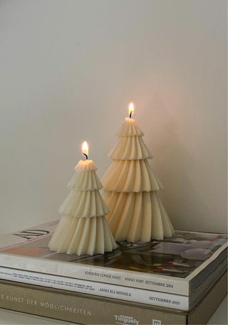 Candele a forma di albero di Natale nelle versioni media e grande, appoggiate su alcuni libri.