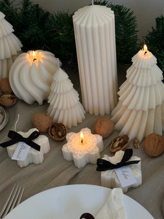 Tre candele a forma di fiocco di neve circondate da candele e decorazioni natalizie.