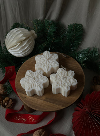 Set da 3 candele a forma di fiocco di neve color Ivory su un vassoio di legno, tra rami di abete e decorazioni natalizie