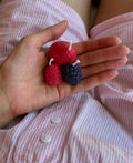 Candele rosse a forma di fragole e lamponi mostrate sul palmo di una mano.