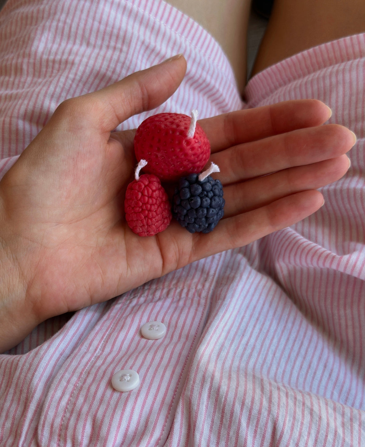 Candele rosse a forma di fragole e lamponi mostrate sul palmo di una mano.