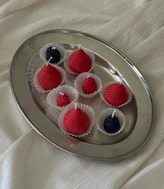 Candele a forma di frutti di bosco disposte in piccoli stampi color crema su un piatto argentato.