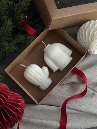 Candele a forma di maglione e muffola in una scatola regalo aperta, con nastro rosso.