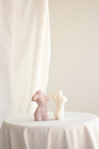 Due candele Muse a forma di busto femminile, una Dusty Pink e una avorio, affiancate su una tovaglia bianca.