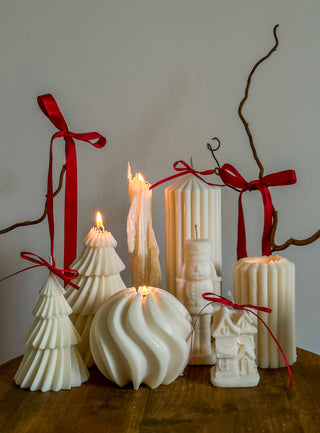 Candela a forma di albero di Natale accesa insieme ad altre candele natalizie in un allestimento festivo.