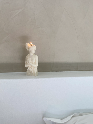 Candela Lady Afrodite Ivory accesa su una mensola bianca davanti a una parete in microcemento