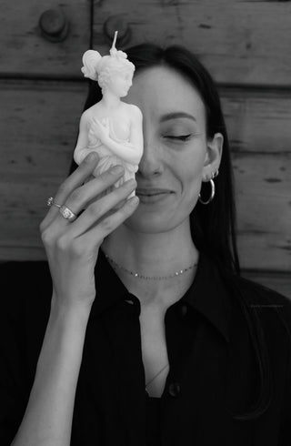Donna sorridente con gli occhi chiusi che tiene accanto al viso la candela Lady Afrodite Ivory, foto in bianco e nero