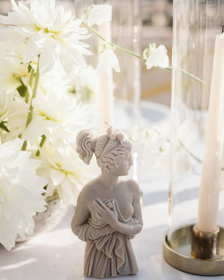 Candela Lady Afrodite Stone Grey su una tavola di matrimonio, accanto a dalie bianche e a una candela lunga in un portacandela di vetro