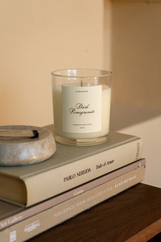 Candela profumata Dark Pomegranate Hot&Vintage in vasetto di vetro con etichetta, appoggiata su dei libri accanto a un piattino in pietra