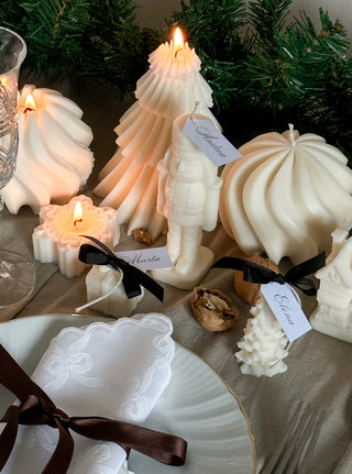 Candele natalizie Ivory su una tavola di Natale: schiaccianoci, alberi, fiocco di neve e pacchetto regalo con nastro nero e cartellini segnaposto