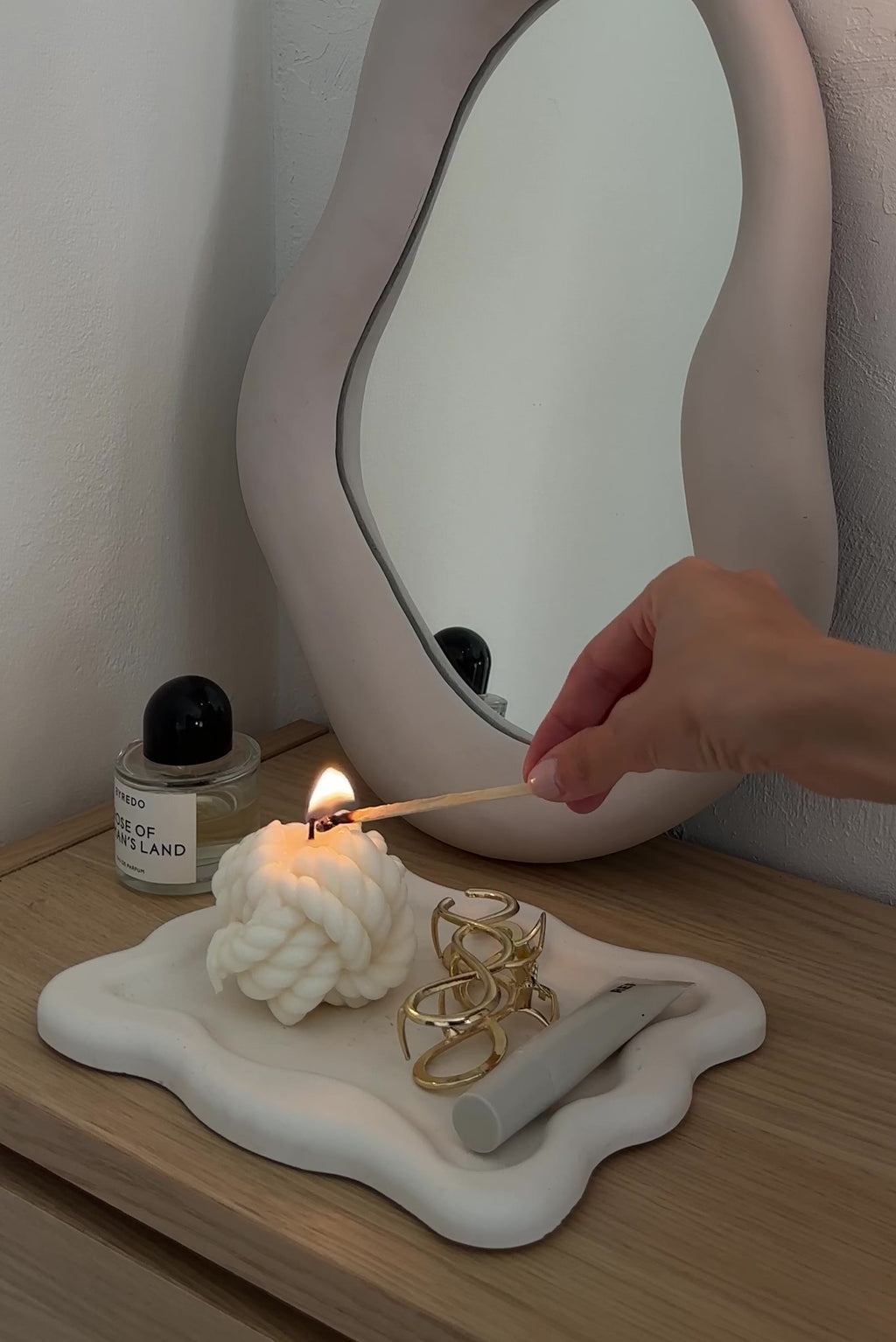 Video della candela a forma di nodo appoggiata su un piattino color crema accanto a uno specchio.