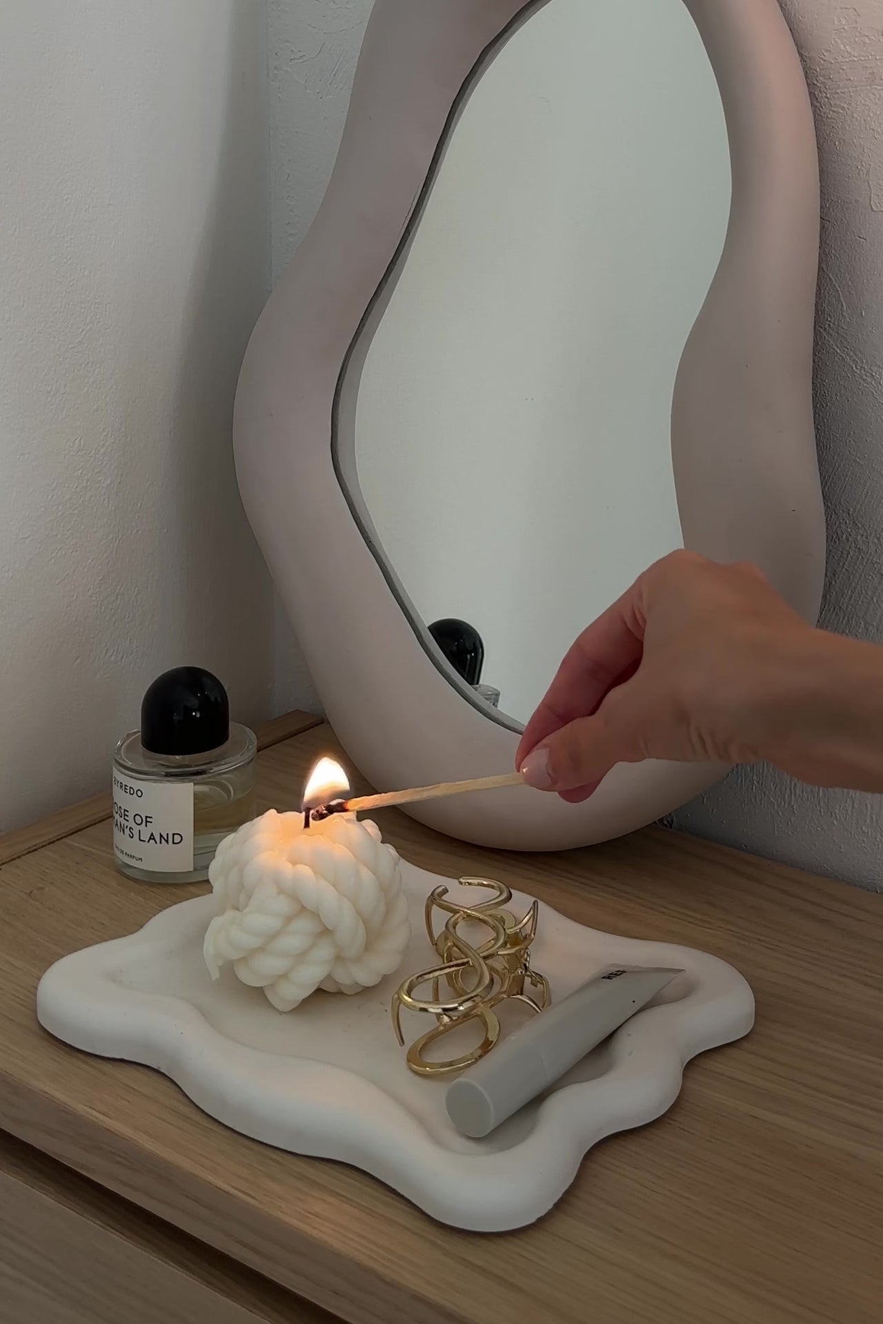 Video della candela a forma di nodo appoggiata su un piattino color crema accanto a uno specchio.
