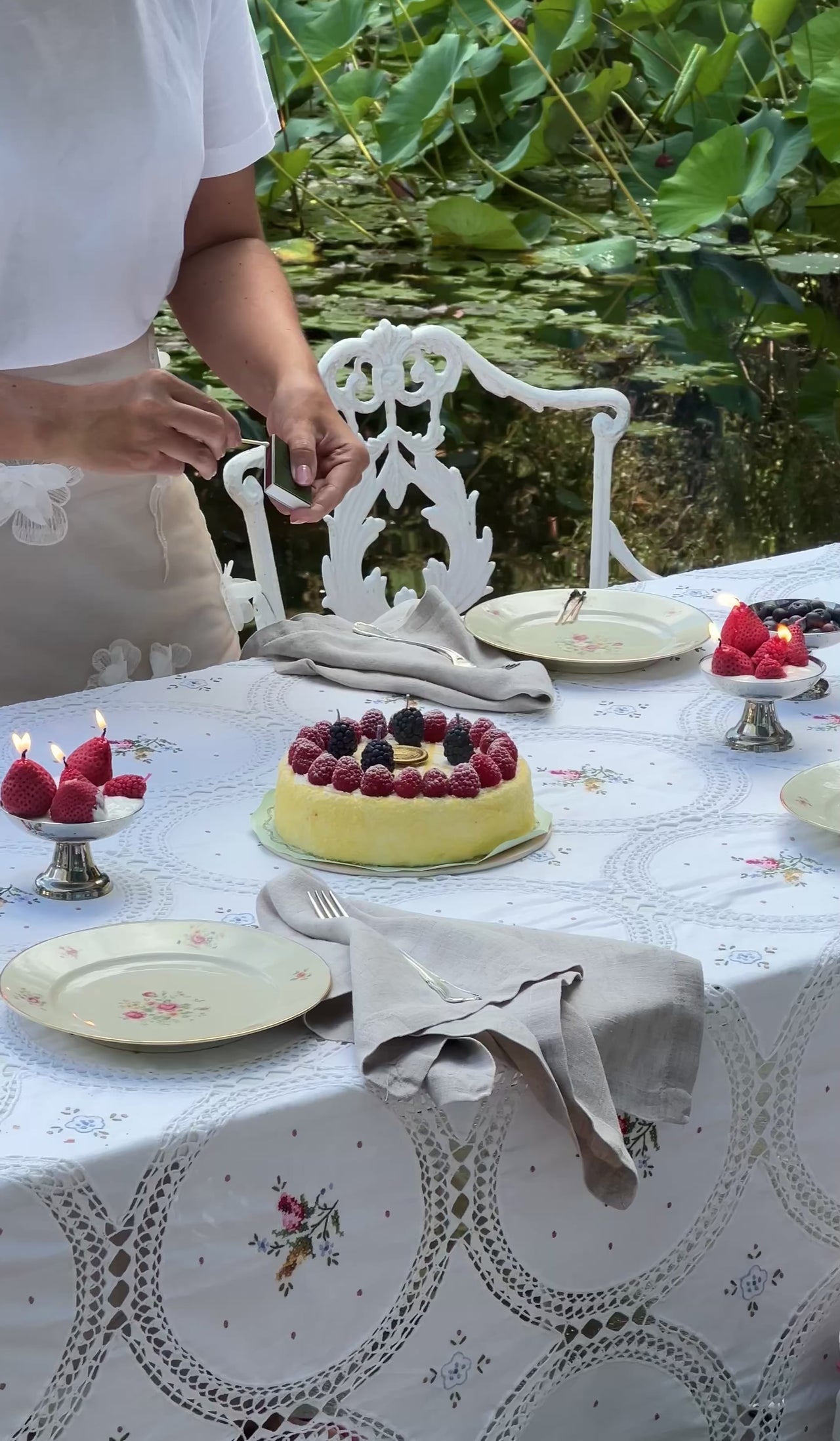 Video di una donna che accende le candeline a forma di frutti di bosco su una torta, su una tavola apparecchiata all'aperto
