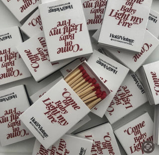 Diverse scatole di fiammiferi “Come On Baby, Light My Fire” sovrapposte, con la scritta rossa visibile.