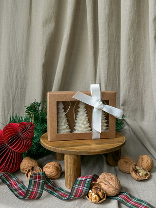 Tre candele color avorio a forma di albero di Natale nella confezione regalo con fiocco bianco, insieme a schiaccianoci e decorazioni natalizie.