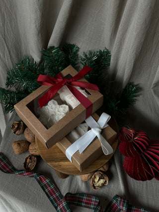Due confezioni regalo del set di candele con fiocco di neve e casetta, una con fiocco rosso e una con fiocco bianco.
