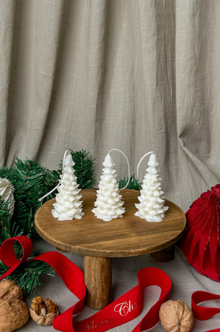 Tre candele color avorio a forma di albero di Natale disposte su piatti, con nastro rosso, schiaccianoci e decorazioni verdi.