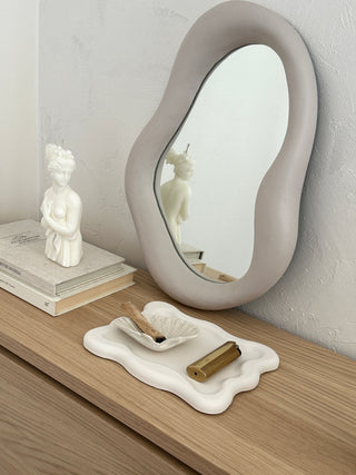 Vassoio quadrato dai bordi ondulati con candela e specchio in un allestimento decorativo.